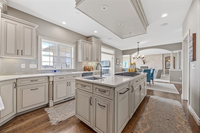 kitchen with tasteful backsplash, dark wood-type flooring, light countertops, an island with sink, and arched walkways