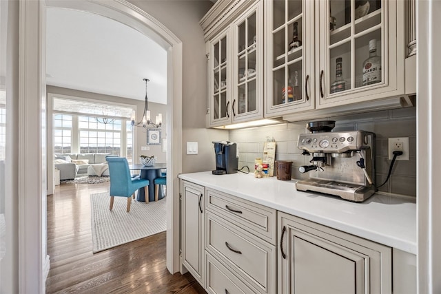 bar with dark wood finished floors, a notable chandelier, arched walkways, and backsplash