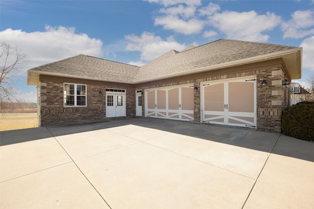 view of front of house featuring driveway, a garage, brick siding, and roof with shingles