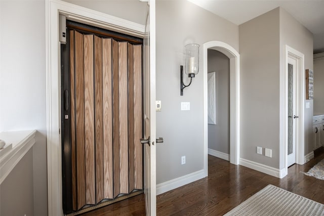 hall featuring arched walkways, dark wood-type flooring, and baseboards