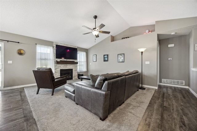 living area featuring visible vents, a ceiling fan, wood finished floors, a stone fireplace, and vaulted ceiling