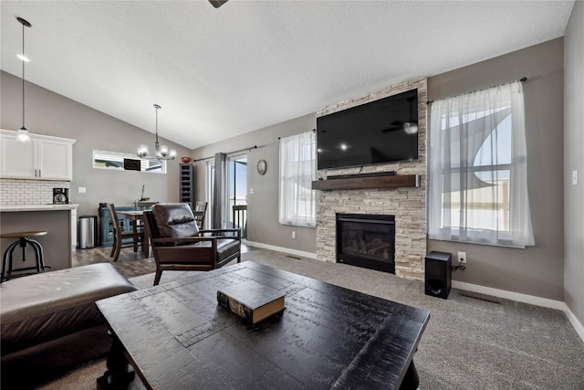 carpeted living room featuring baseboards, vaulted ceiling, a stone fireplace, a notable chandelier, and a textured ceiling