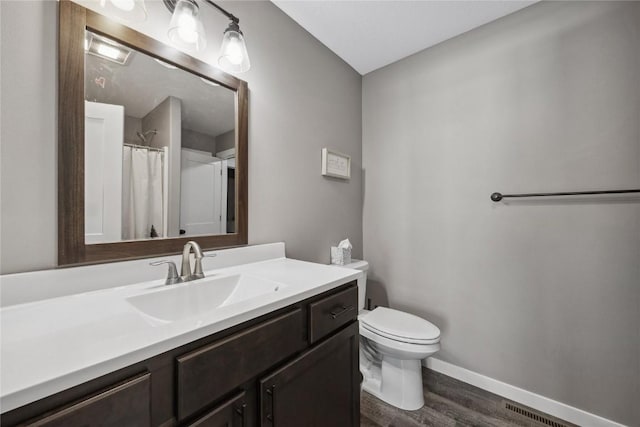 bathroom with vanity, wood finished floors, baseboards, visible vents, and toilet