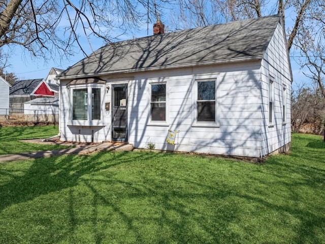 view of front facade with a chimney, a front yard, and roof with shingles