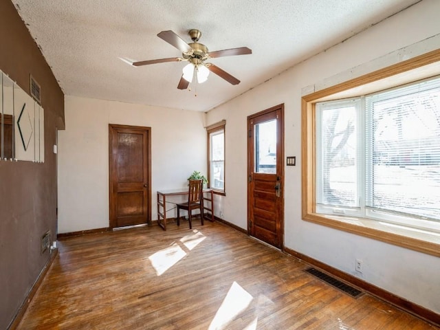 foyer featuring a textured ceiling, wood finished floors, visible vents, and a healthy amount of sunlight