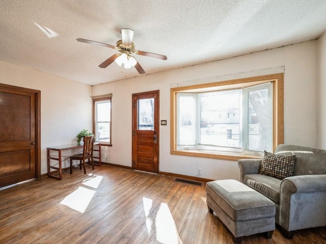 entryway with a ceiling fan, wood finished floors, visible vents, baseboards, and a textured ceiling