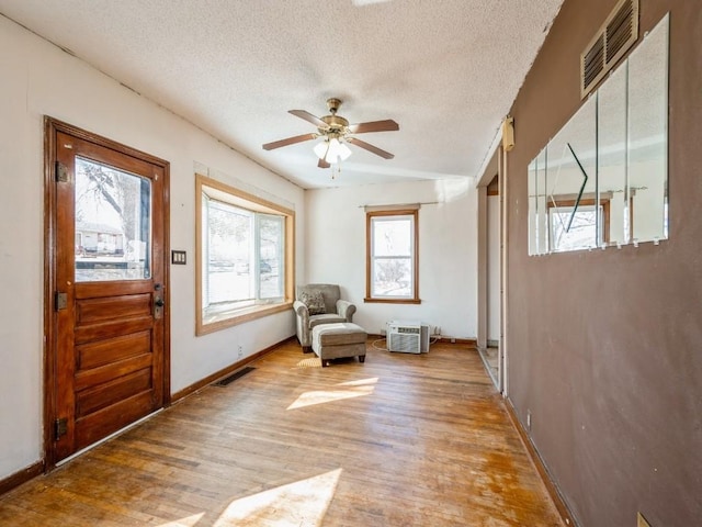 living area featuring a ceiling fan, visible vents, light wood finished floors, and a textured ceiling