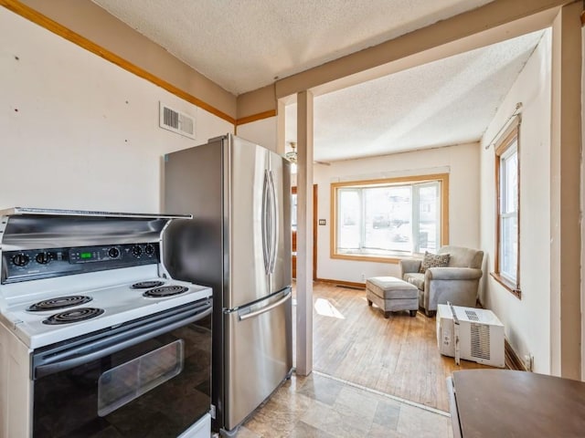 kitchen with a wall mounted air conditioner, visible vents, white electric range, a textured ceiling, and freestanding refrigerator