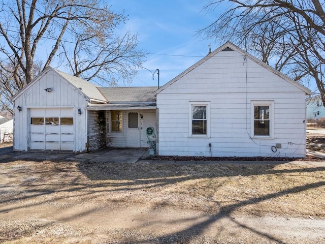 view of front facade with an attached garage, a shingled roof, and dirt driveway