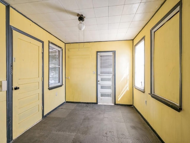 empty room with baseboards, wood walls, and dark carpet