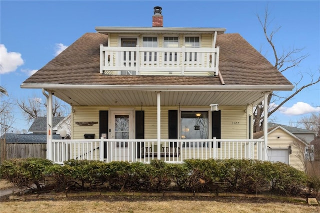 view of front facade with a balcony, roof with shingles, covered porch, and a chimney