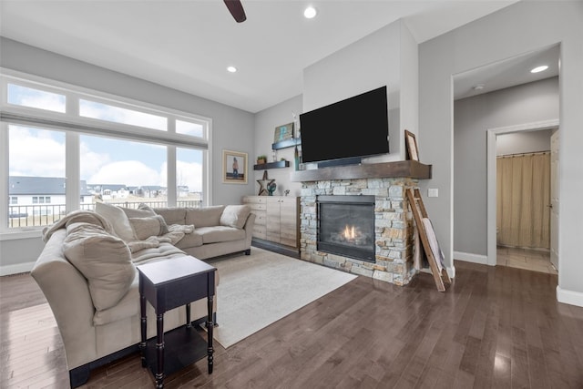 living area featuring dark wood-type flooring, baseboards, a stone fireplace, recessed lighting, and a ceiling fan