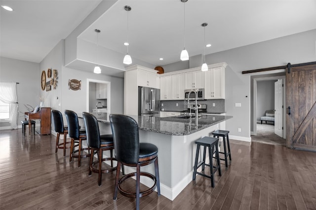 kitchen featuring dark wood-type flooring, a breakfast bar area, a barn door, decorative backsplash, and stainless steel appliances