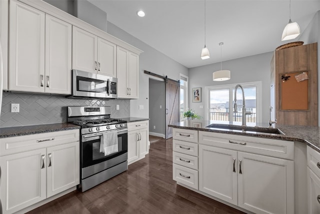 kitchen featuring a sink, backsplash, white cabinetry, a barn door, and appliances with stainless steel finishes