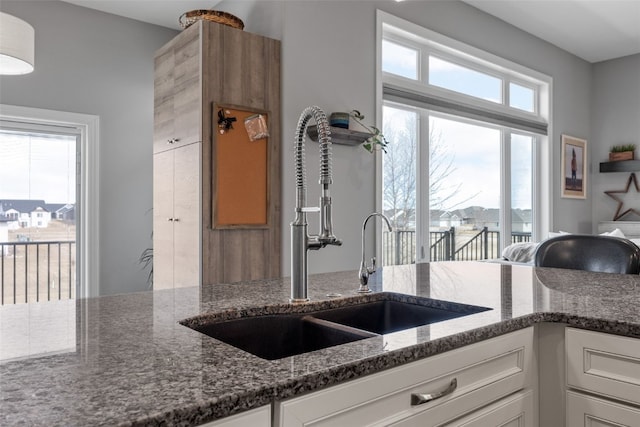 kitchen featuring dark stone counters, white cabinets, and a sink