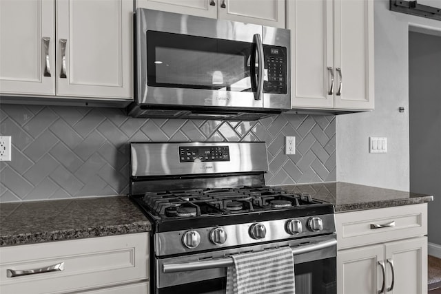 kitchen with backsplash, appliances with stainless steel finishes, white cabinetry, and dark stone counters