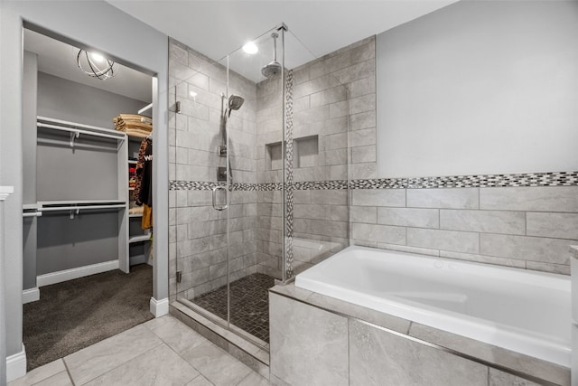 full bathroom featuring a bath, a stall shower, a spacious closet, and baseboards