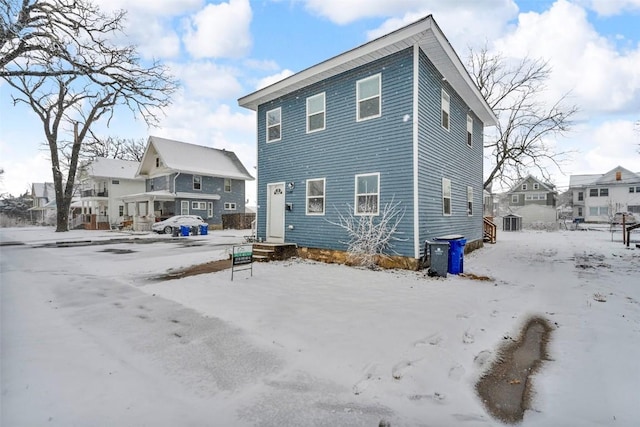 snow covered back of property featuring a residential view and entry steps