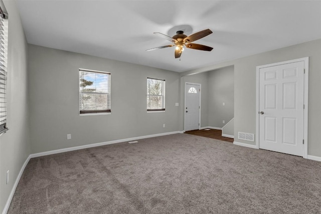 empty room with dark colored carpet, visible vents, baseboards, and ceiling fan