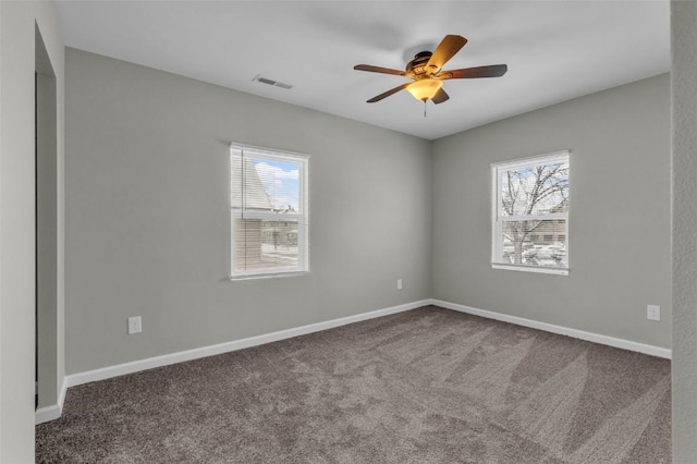 carpeted spare room featuring plenty of natural light, baseboards, visible vents, and a ceiling fan