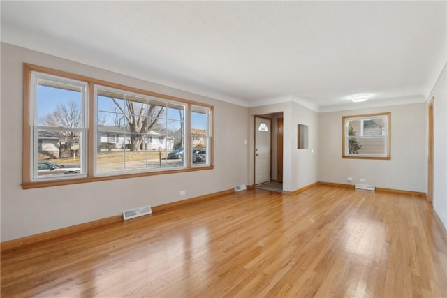 unfurnished living room with light wood finished floors, visible vents, and baseboards