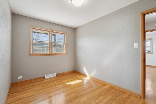 spare room featuring wood finished floors, visible vents, and baseboards