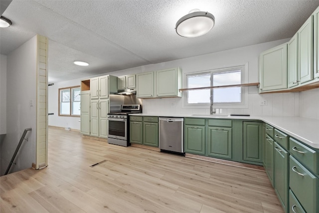 kitchen with green cabinets, light wood finished floors, appliances with stainless steel finishes, and a sink