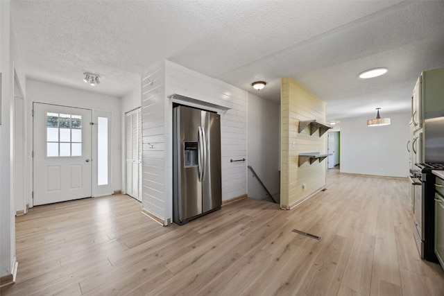 kitchen with wooden walls, light wood-style floors, appliances with stainless steel finishes, and a textured ceiling