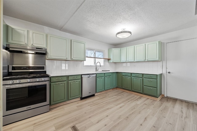 kitchen with a sink, stainless steel appliances, under cabinet range hood, green cabinets, and light wood-type flooring