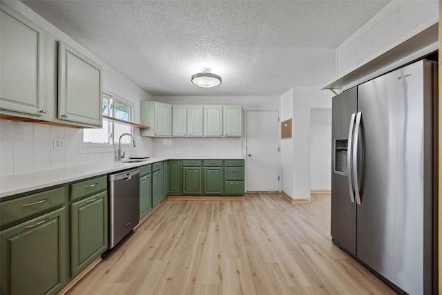 kitchen featuring light wood finished floors, green cabinetry, decorative backsplash, stainless steel appliances, and a sink