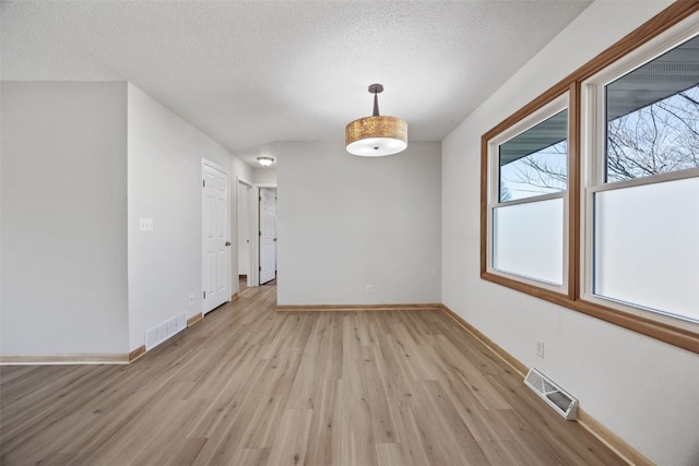 unfurnished room with light wood finished floors, visible vents, a textured ceiling, and baseboards