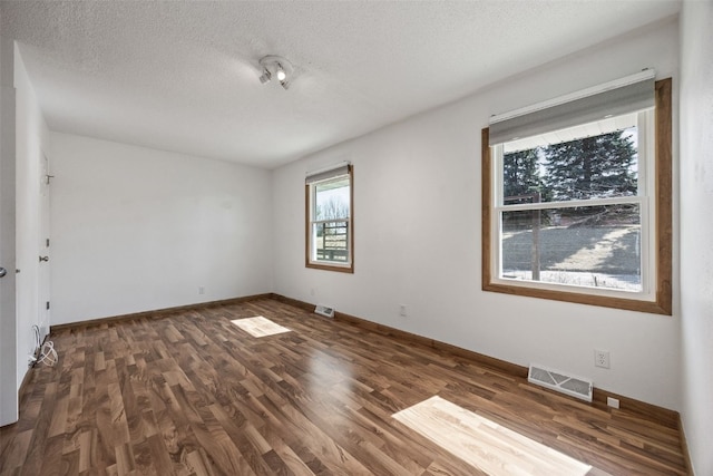 spare room featuring visible vents, a textured ceiling, baseboards, and wood finished floors