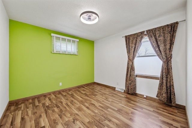 spare room with baseboards, wood finished floors, visible vents, and a textured ceiling