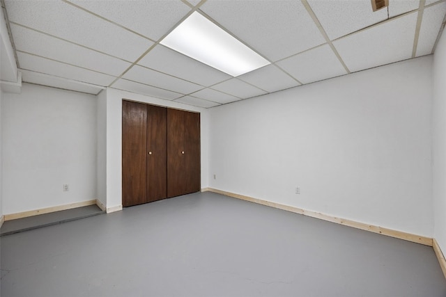 unfurnished bedroom with a closet, a paneled ceiling, baseboards, and concrete flooring