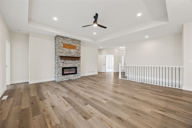 unfurnished living room featuring a stone fireplace, a tray ceiling, recessed lighting, and wood finished floors