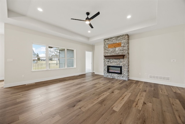 unfurnished living room featuring visible vents, a stone fireplace, wood finished floors, a raised ceiling, and a ceiling fan