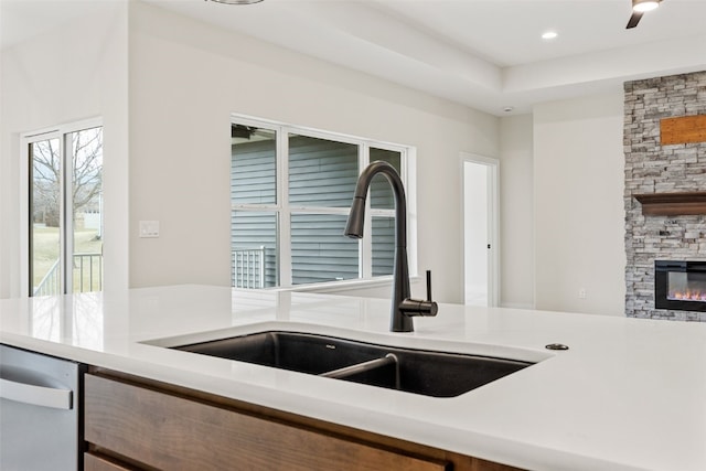 kitchen featuring a sink, light countertops, a stone fireplace, recessed lighting, and stainless steel dishwasher