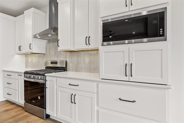 kitchen with wall chimney range hood, backsplash, white cabinetry, stainless steel appliances, and light countertops