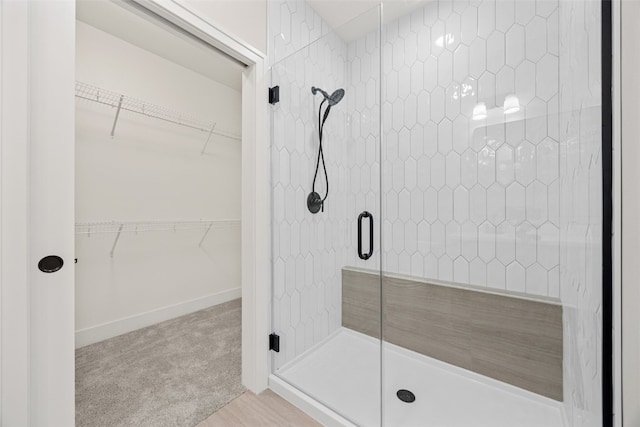 bathroom with a walk in closet, a shower stall, and baseboards