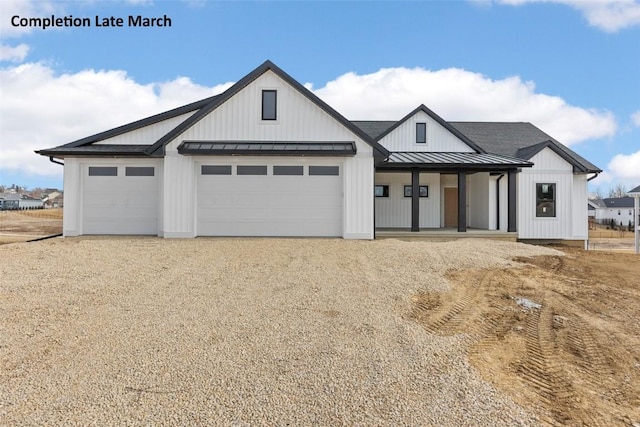 modern farmhouse with a garage, metal roof, gravel driveway, and a standing seam roof