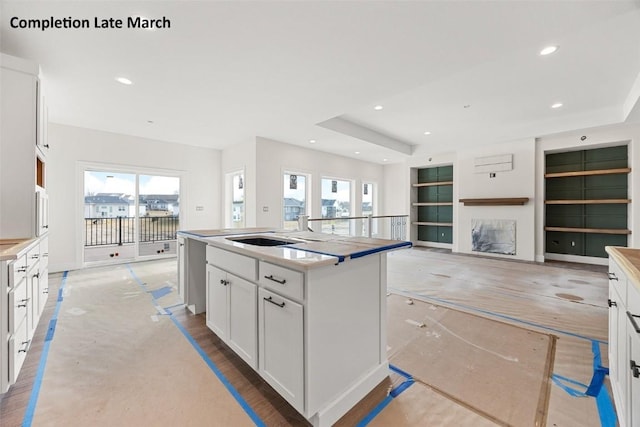 kitchen with built in shelves, a fireplace, recessed lighting, a kitchen island with sink, and white cabinetry