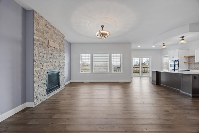 unfurnished living room featuring baseboards, a stone fireplace, and dark wood-style floors