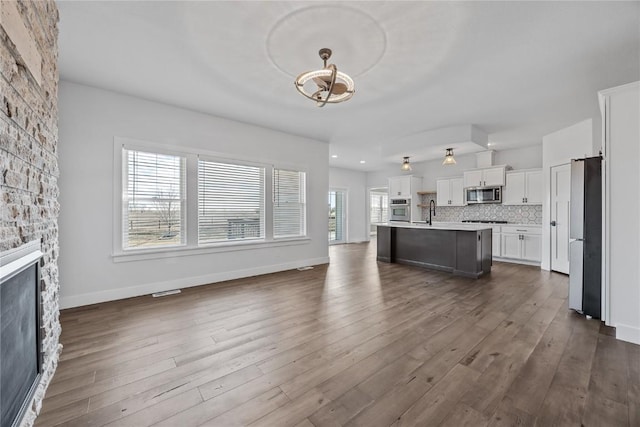 kitchen featuring backsplash, open floor plan, an island with sink, a fireplace, and stainless steel appliances