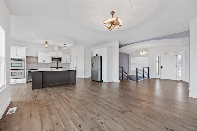 kitchen featuring wood finished floors, light countertops, appliances with stainless steel finishes, open floor plan, and backsplash