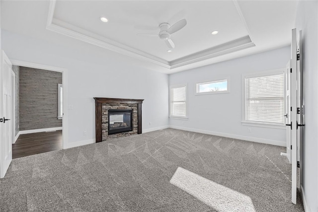 unfurnished living room with a stone fireplace, a raised ceiling, baseboards, and carpet floors