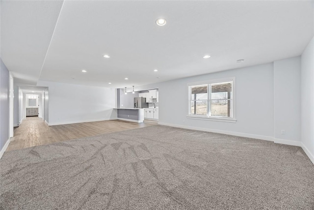 unfurnished living room with recessed lighting, light wood-style floors, baseboards, and light colored carpet