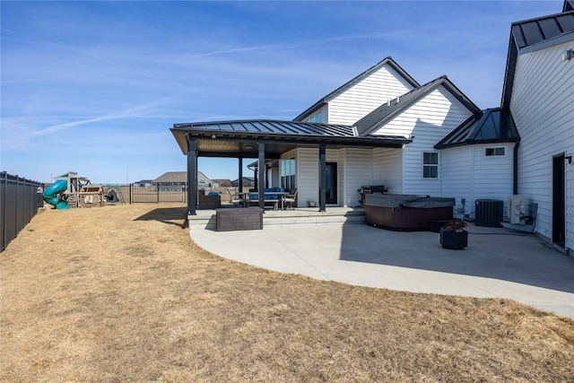 back of house with a hot tub, a playground, a standing seam roof, metal roof, and a patio