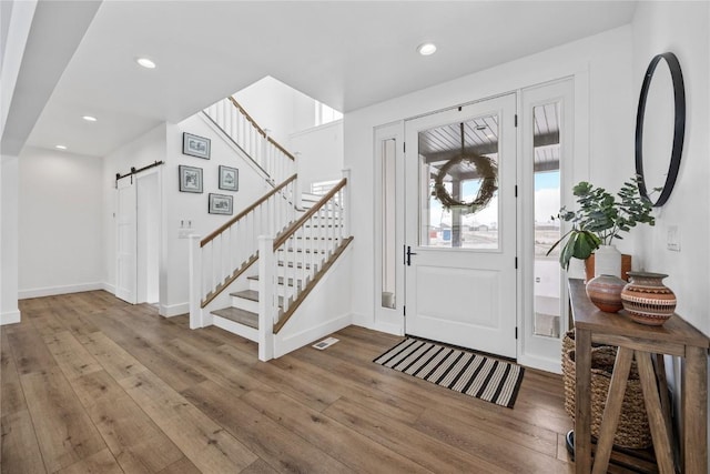 foyer featuring hardwood / wood-style floors, a barn door, stairway, and visible vents