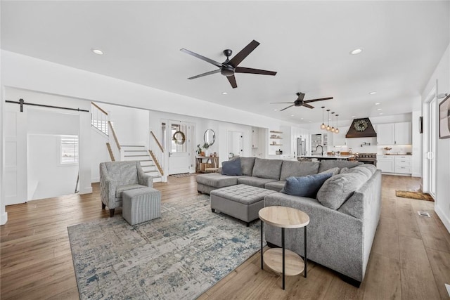 living area with ceiling fan, stairway, light wood-type flooring, a barn door, and recessed lighting