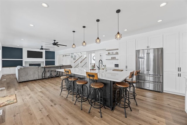 kitchen with a breakfast bar, high end fridge, light countertops, white cabinets, and light wood-type flooring